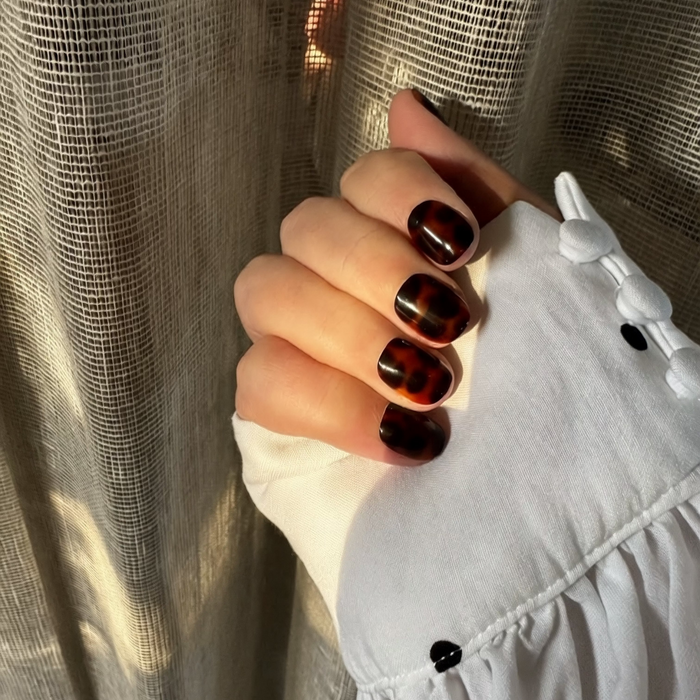 Hand with tortoiseshell Instant Mani press on nails against a textured beige background