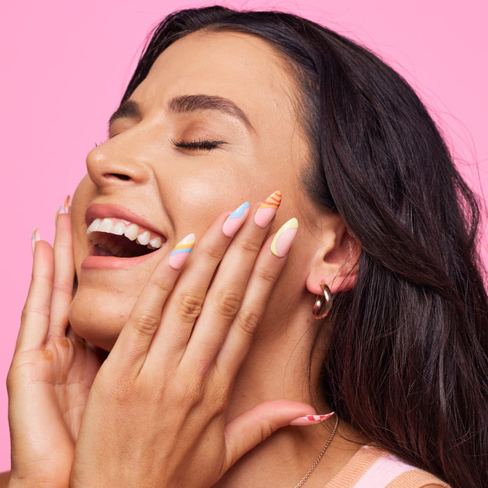 Girl smiling standing in front of pink background wearing Instant Mani Co. Carnival colourful press on nails.