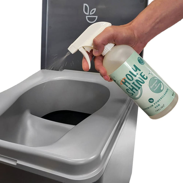 Eine Hand sprüht biologisch abbaubaren Trenntoiletten-Reiniger auf einen Toilettenrand.
