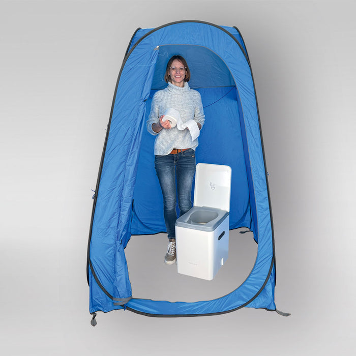 Frau in einem blauen Pop Up-Toilettenzelt mit weißer Toilette, die Toilettenpapier hält.