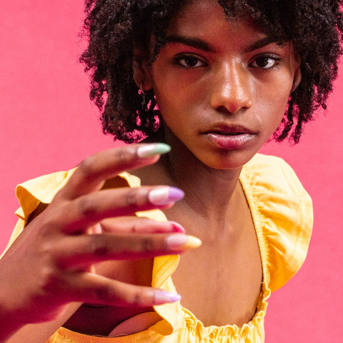 Girl wearing yellow top, with Instant Mani Co. rainbow coloured tip press-on nails